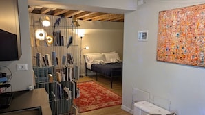 A bedroom with a bed, a red rug, a wall art piece, and a ceiling with exposed beams. - Piccola Perla sul canale (Venezia)