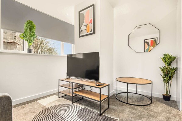 A modern living room with a flat-screen TV, a round wooden table, a potted plant, and abstract wall art. - Stylish 1 BED Apartment in Central Hull (Kingston upon Hull)