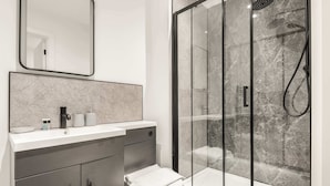 Un bany modern amb una cabina de dutxa de vidre, un lavabo blanc i un mirall gran.