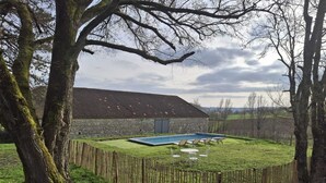 Ein Steinhaus mit Swimmingpool, umgeben von einem Holzzaun und Bäumen.