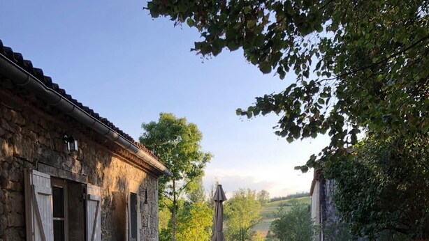 Ein Kiesweg führt zu einem Steinhaus mit Tisch und Stühlen vor der Fassade.