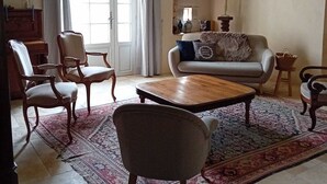 Ein Wohnzimmer mit Sofa, Sesseln, einem Couchtisch, einer Chandelierleuchtre, einem Teppich und einem fenster mit Vorhängen.