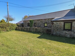 A stone building with a sloped roof, a wooden fence, and a grassy yard. - Butterslade (Swansea)