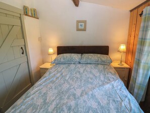 A bedroom with a bed, two bedside tables with lamps, a wooden headboard, a wall-mounted picture, and a wooden door with a geometric design. - Butterslade (Swansea)