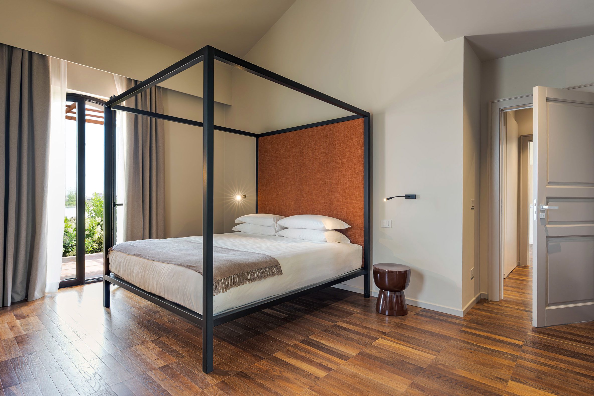 Una cama con dosel, un cabecero, una mesita redonda y una puerta que da a otra habitación.