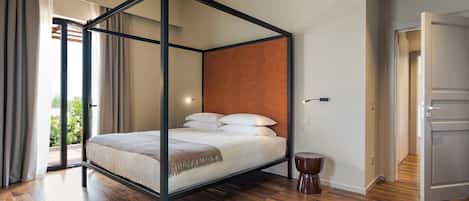 A four-poster bed with a headboard, a small round table, and a door leading to another room.