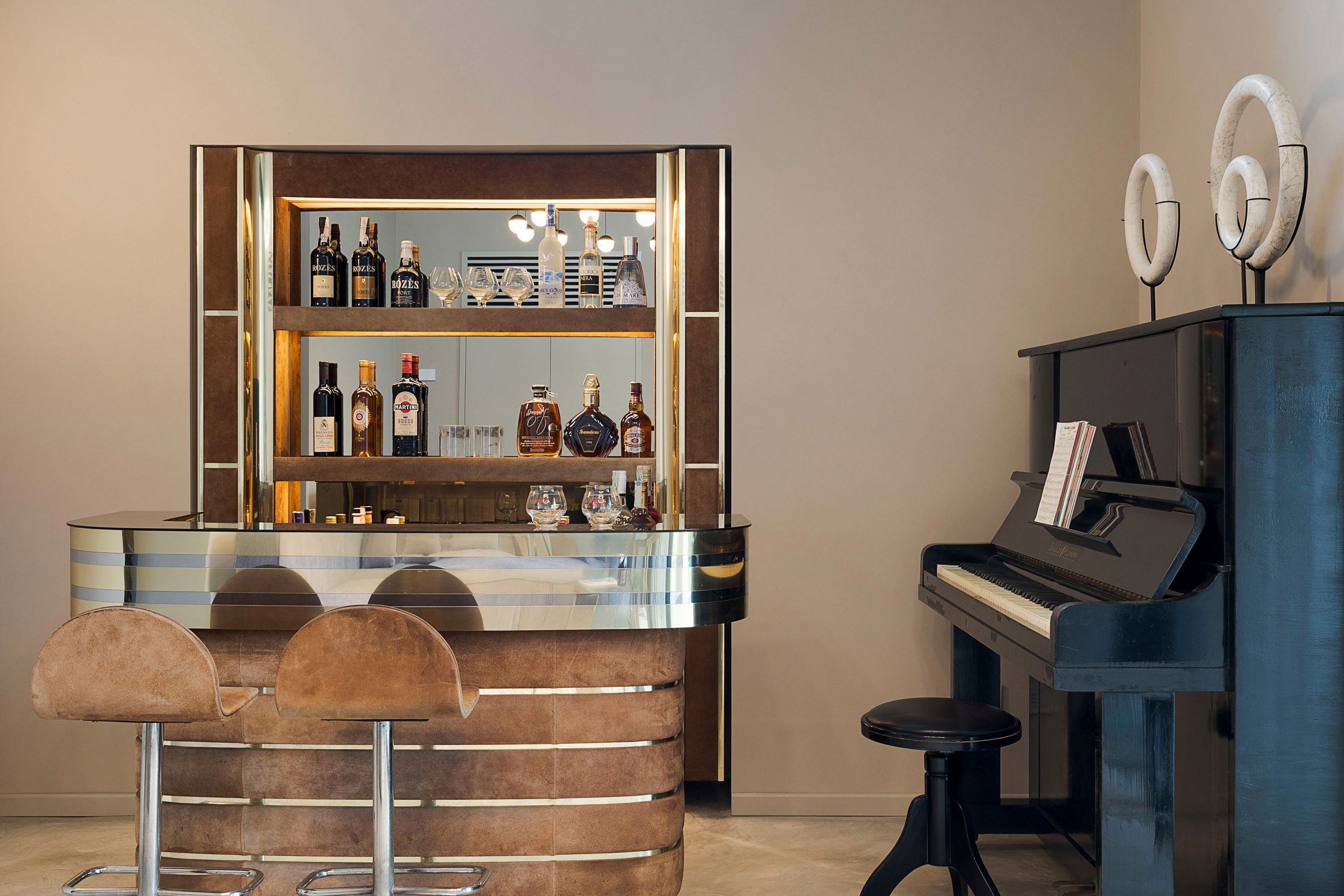 Een bar met een piano en krukken, met verschillende soorten drankflessen en glazen.