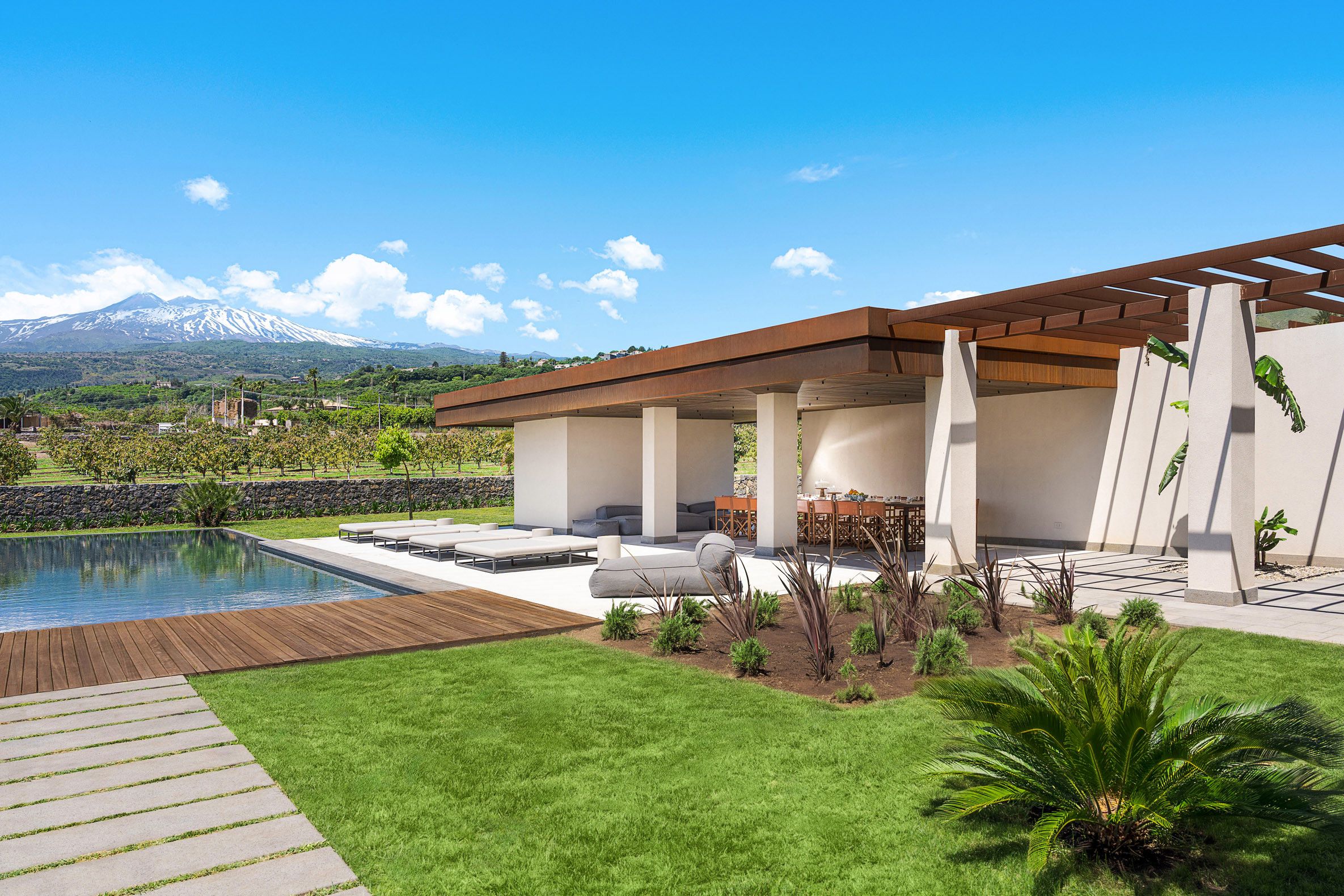 A modern outdoor patio with a pool, seating, and a view of a mountain.