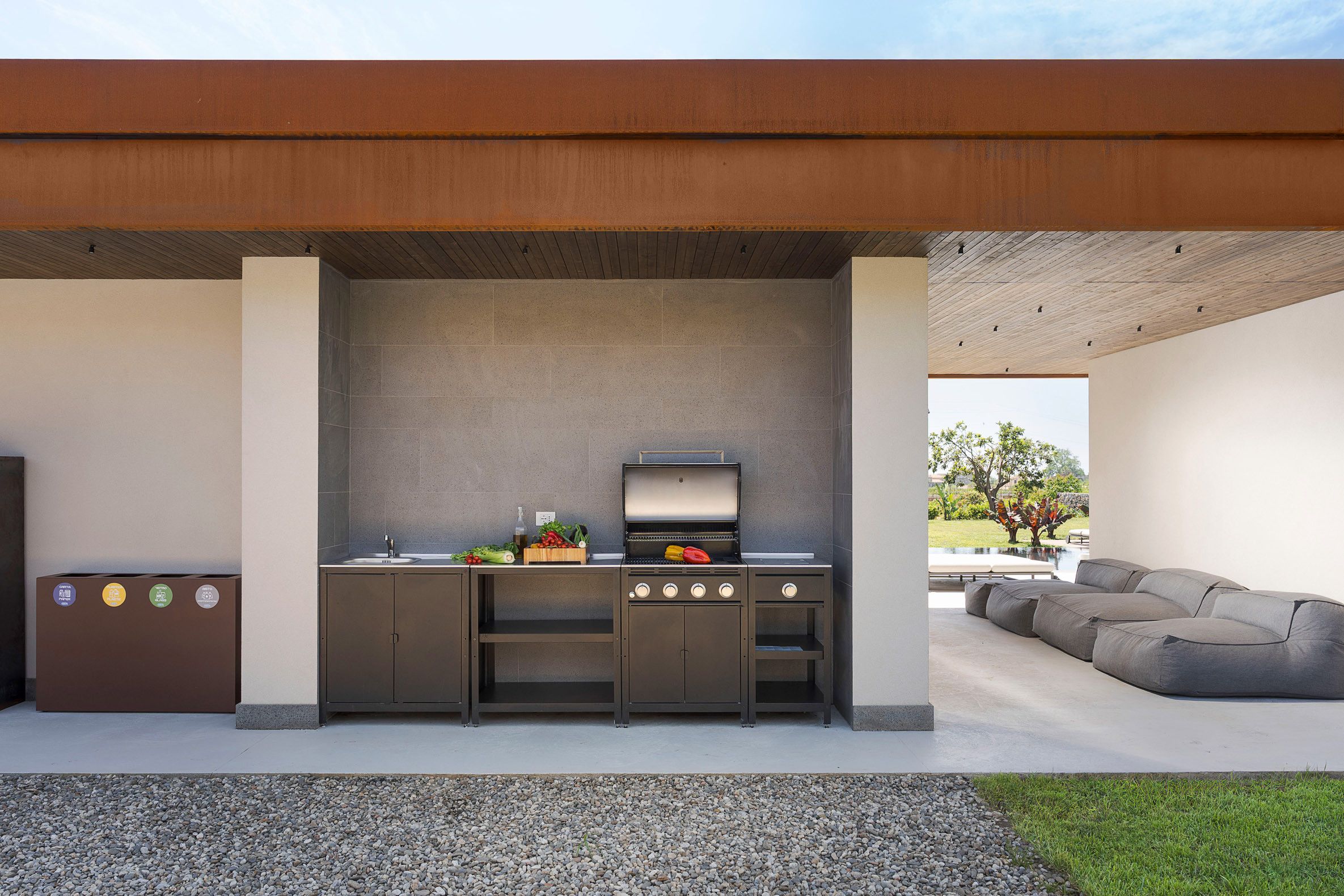 An outdoor kitchen with a grill, sink, and storage cabinets, adjacent to a modern outdoor seating area.