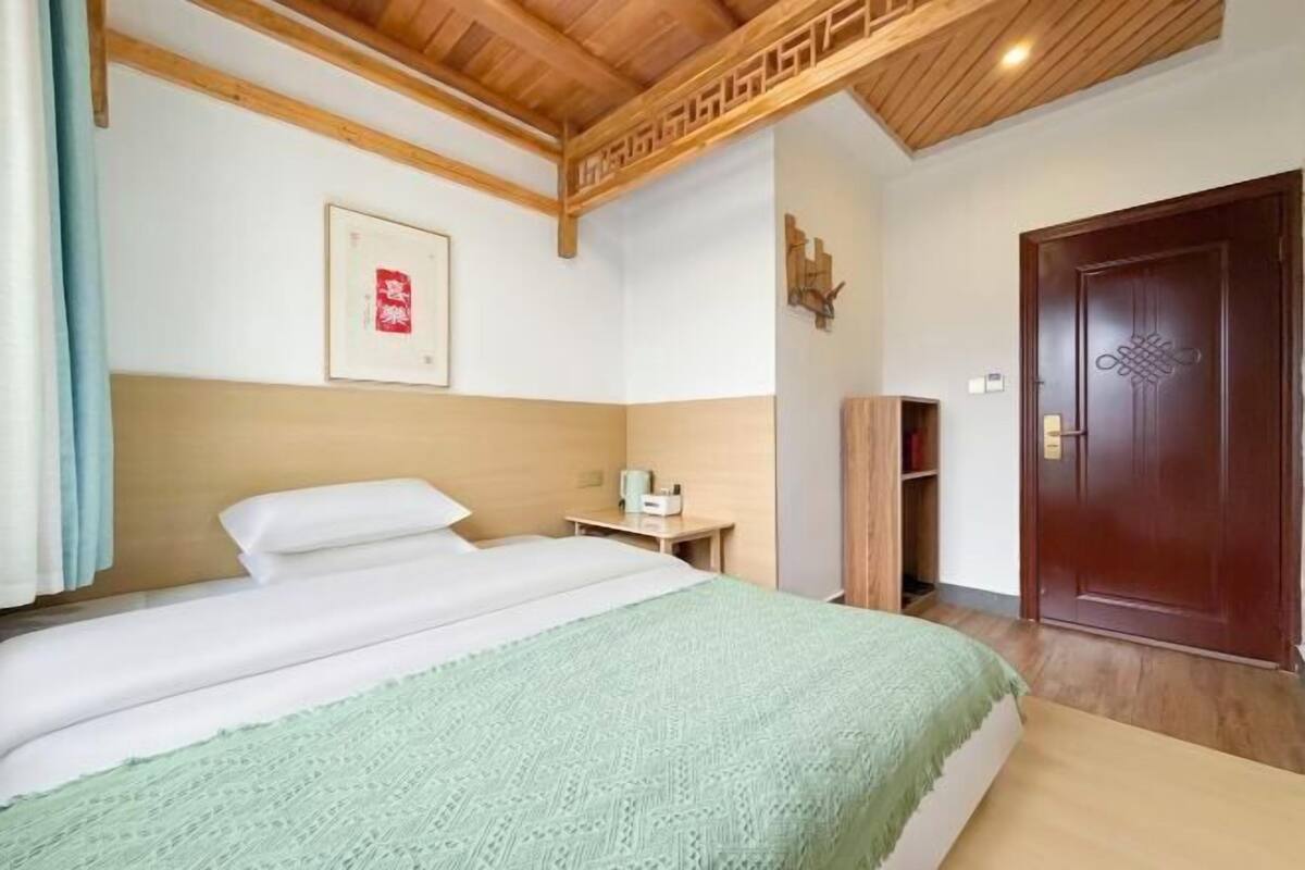 A hotel room with a bed, a bedside table, a wall-mounted artwork, and a wooden door.