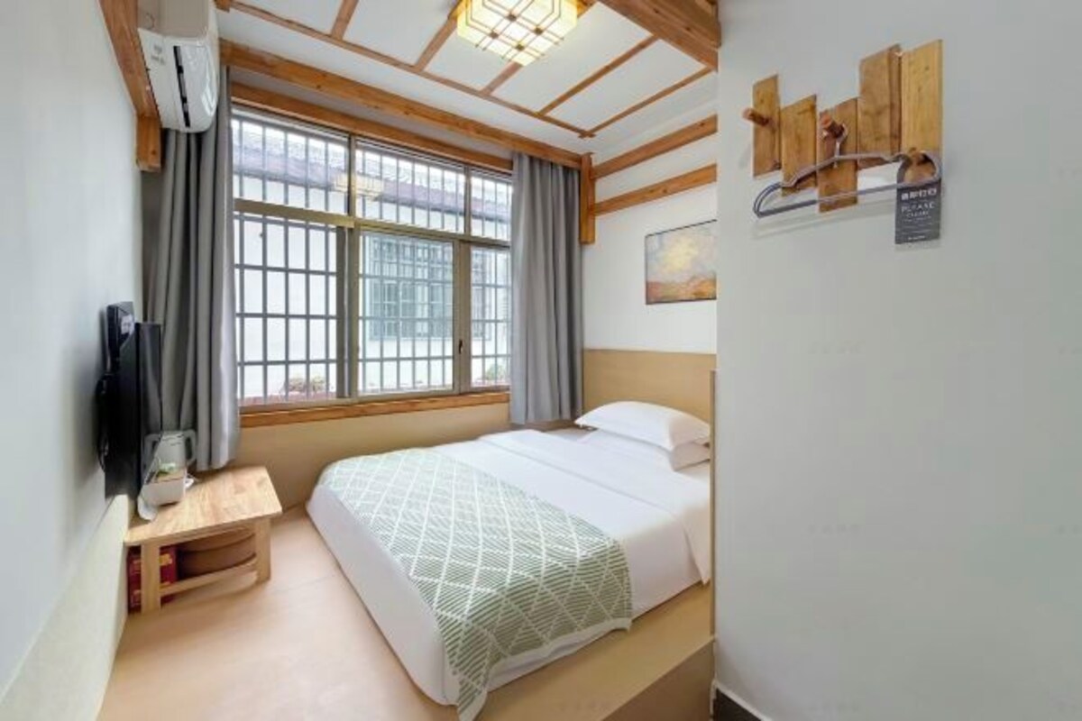 Un dormitorio con cama, ventana, mesita de noche y lámpara de pared.