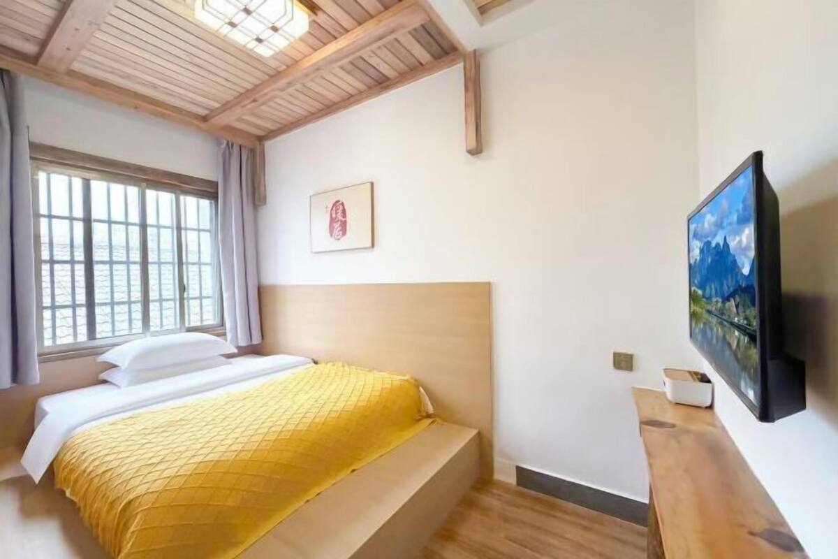 A hotel room with a bed, a window, a painting, and a television.