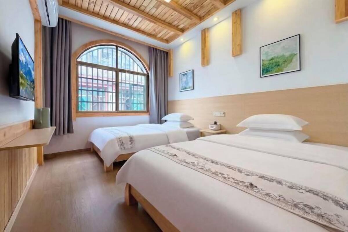 A hotel room with two beds, a large arched window, wooden ceiling beams, and artwork on the walls.