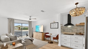 A modern living room with a sofa, coffee table, and a dining area with a table and chairs. There is a kitchen with white cabinets and a stainless steel refrigerator. - Endless Escape A10-Beach Access-Sleeps 2 (Panama City Beach)