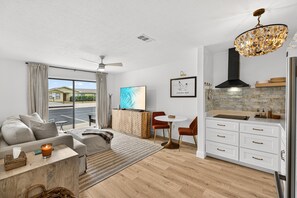 Ein modernes Wohnzimmer mit einer Couch, einem Couchtisch und einem Essbereich mit Tisch und Stühlen. Es gibt eine Küche mit weißen Schränken und einem Edelstahl-Kühlschrank.