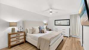 A bedroom with a bed, bedside tables, a ceiling fan, a large mirror, and a painting on the wall. - Endless Escape A10-Beach Access-Sleeps 2 (Panama City Beach)
