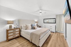 Ein Schlafzimmer mit Bett, Nachttischen, Deckenventilator, einem großen Spiegel und einem Gemälde an der Wand.
