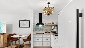 A modern kitchen with white cabinetry, a black range hood, a round dining table with chairs, and a unique chandelier. - Endless Escape A10-Beach Access-Sleeps 2 (Panama City Beach)