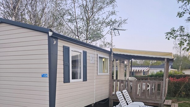 Ein Wohnmobil mit der Aufschrift '124', eine überdachte Veranda mit zwei weißen Loungesesseln und eine kleine Terrassenfläche.