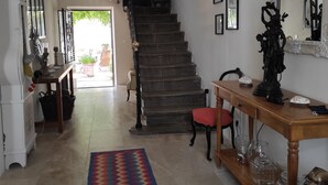 Eine Treppe führt zu einer oberen Etage, ein Holzkonsolentisch mit Dekorationsobjekten, ein gemustertes Teppich und ein großer Spiegel.