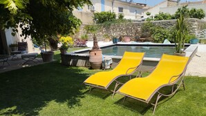 Ein Poolbereich mit gelben Liegestühlen, einer Steinwand und einem kleinen Garten mit Blumentöpfen.