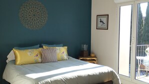 Ein Schlafzimmer mit einem Bett, einer Bank, einer Wanddekoration, einem Bild und einem Fenster.