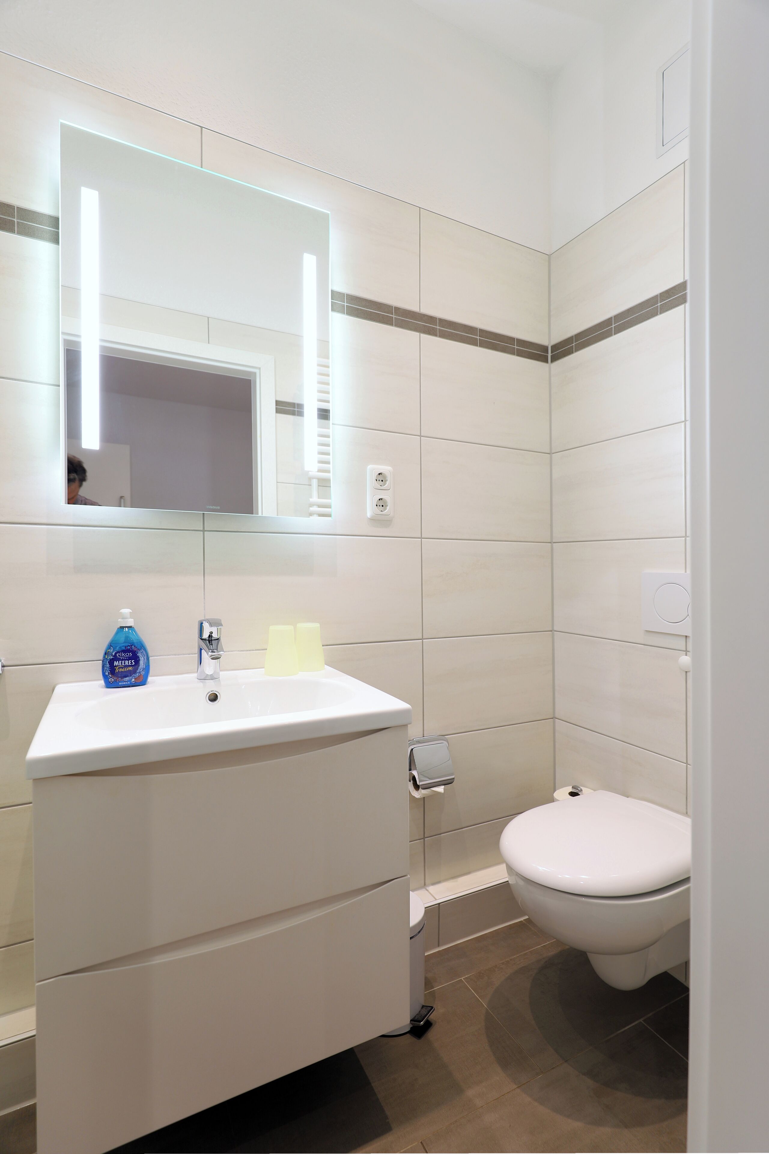 Une salle de bain avec un lavabo, un miroir et des toilettes, le tout de couleur blanche.