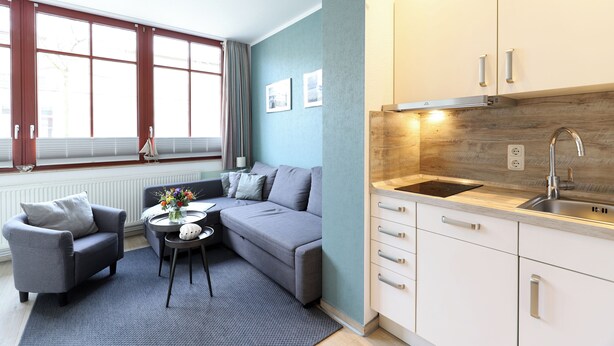 A modern living room with a sofa, armchair, and coffee table, adjacent to a kitchen with a sink and wooden backsplash. - Appartement Nr. 08 (Rostock)