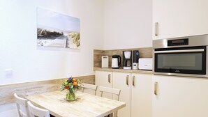 A kitchen with a wooden table, chairs, a coffee maker, a toaster, and an oven. - Appartement Nr. 08 (Rostock)