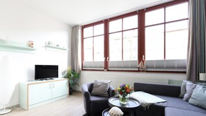 A modern living room with a sofa, armchair, TV, and a small table with a vase. - Appartement Nr. 08 (Rostock)
