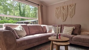 A cozy living room with a large window, a patterned rug, a wooden coffee table, and a macrame wall hanging.
