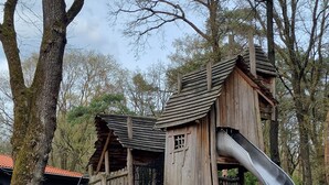 A wooden playhouse with a slide, surrounded by trees.
