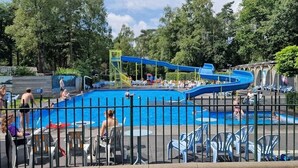 A swimming pool with a slide, surrounded by chairs and a fence.