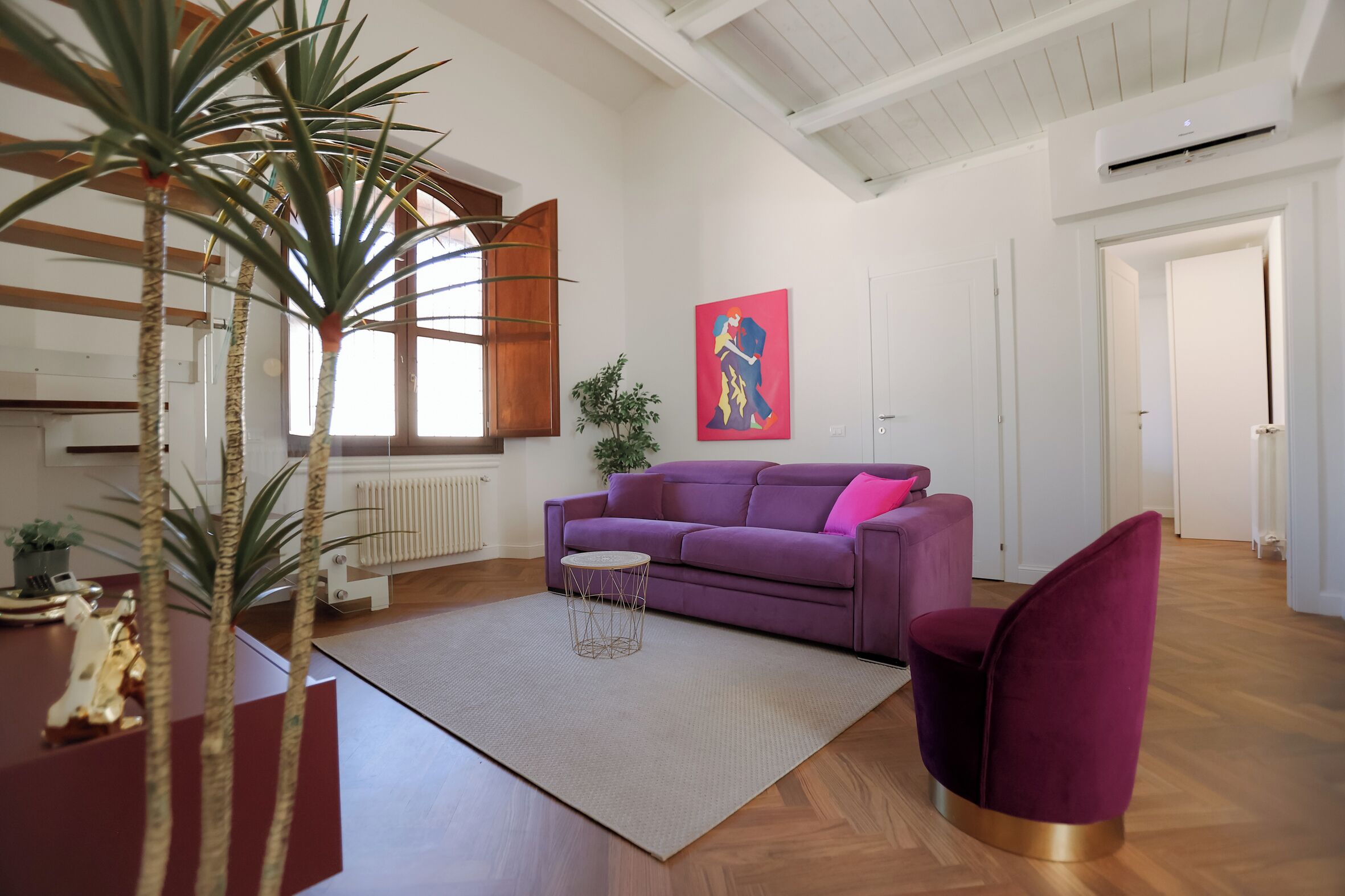 Una sala moderna con un sofá morado, una mesa de centro redonda y un ventanal grande.
