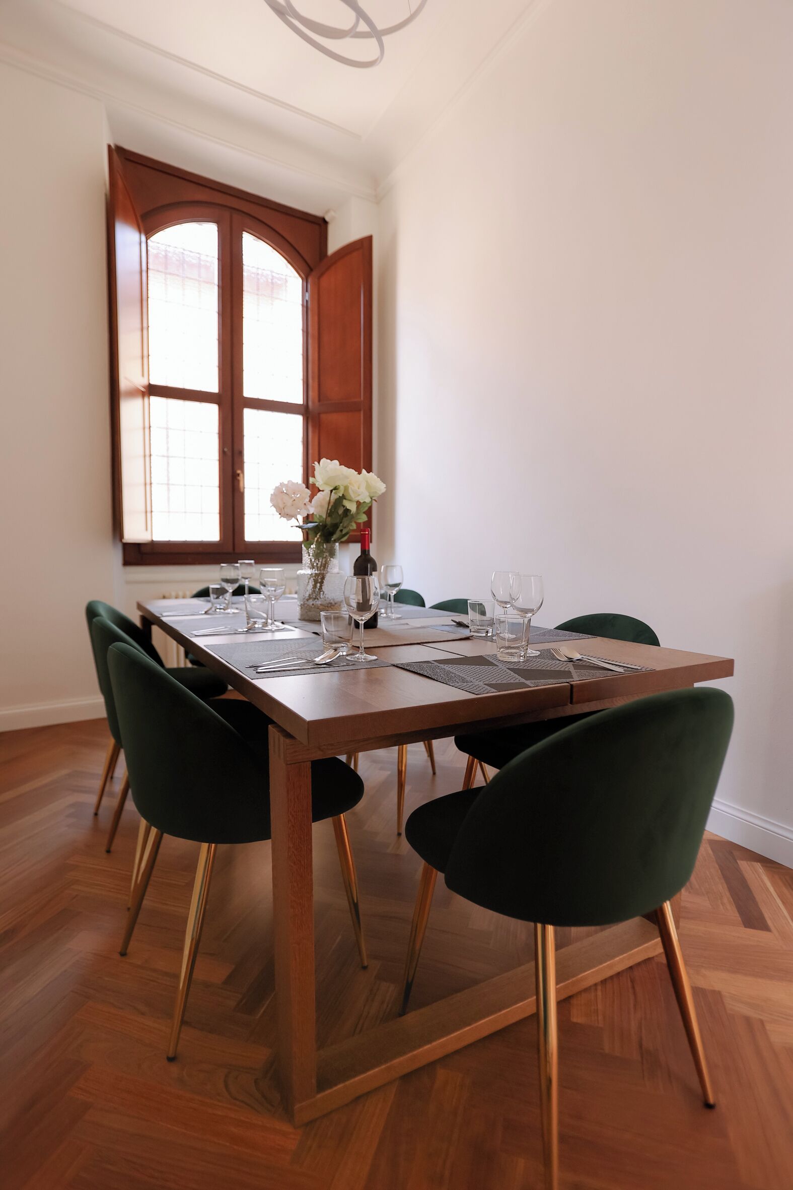 A dining area with a wooden table, green chairs, and a vase with flowers.