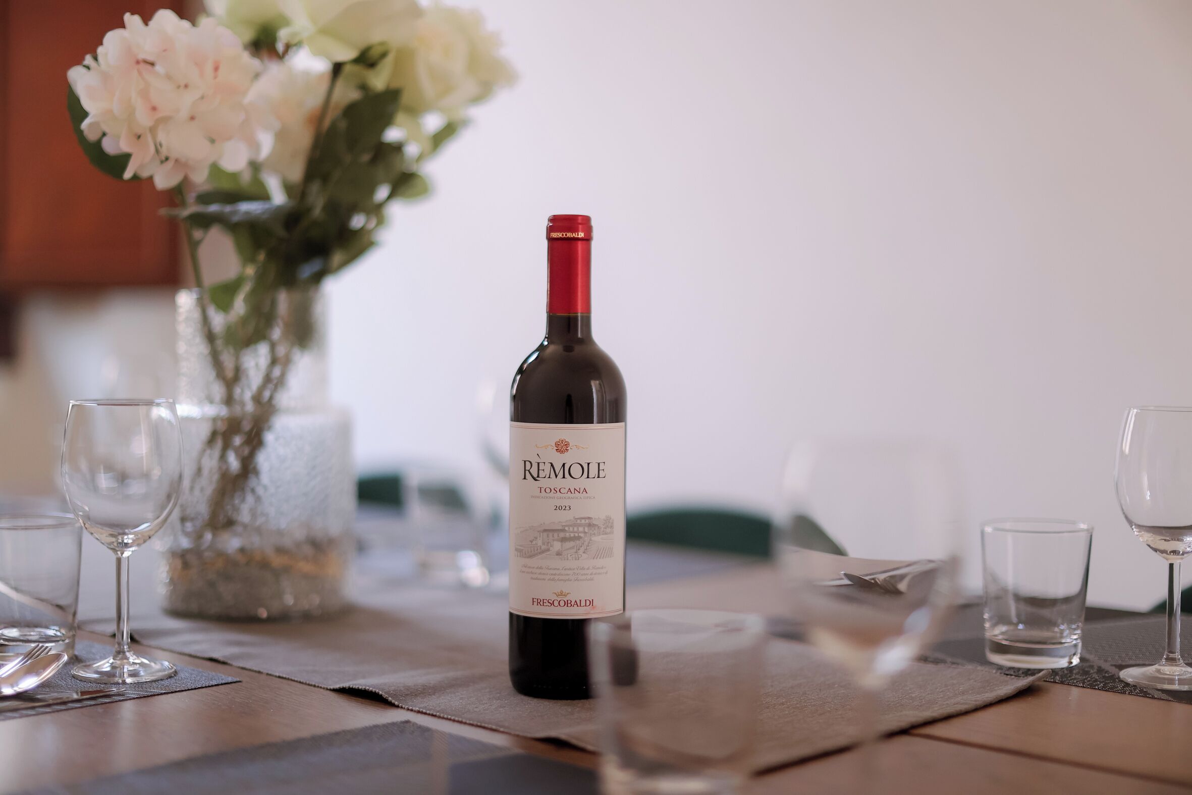 Una bottiglia di vino su un tavolo con bicchieri e un vaso di fiori.