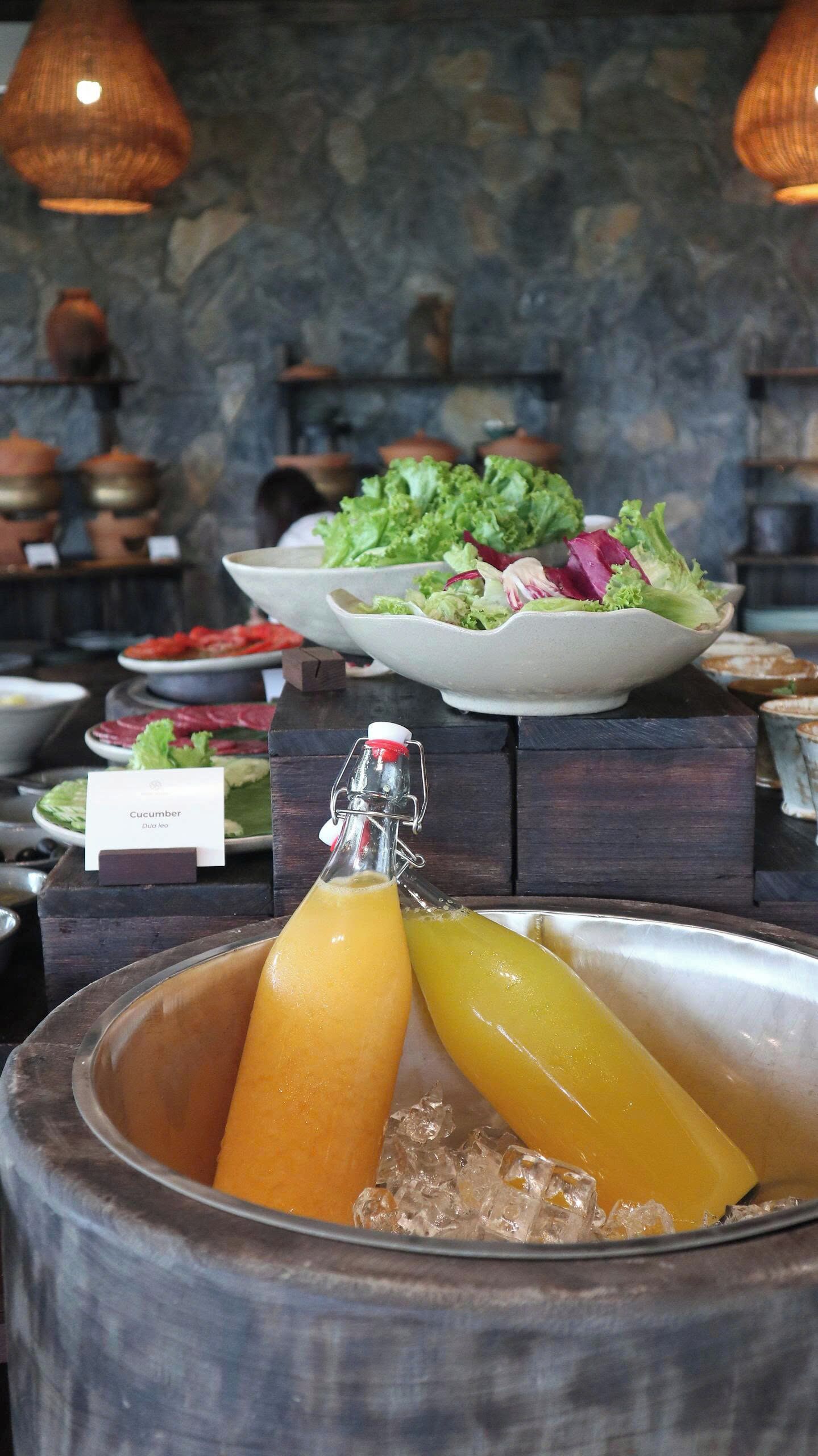 Un bufé con diversos platos, incluyendo un tazón de ensalada, una botella de jugo y un letrero que dice 'Pepino'.