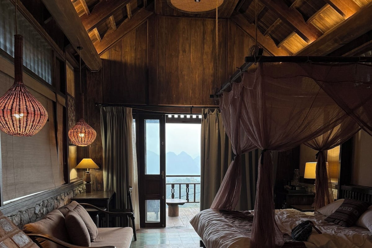 Quarto com teto de madeira, cama com dossel, sofá e mesa com abajur.