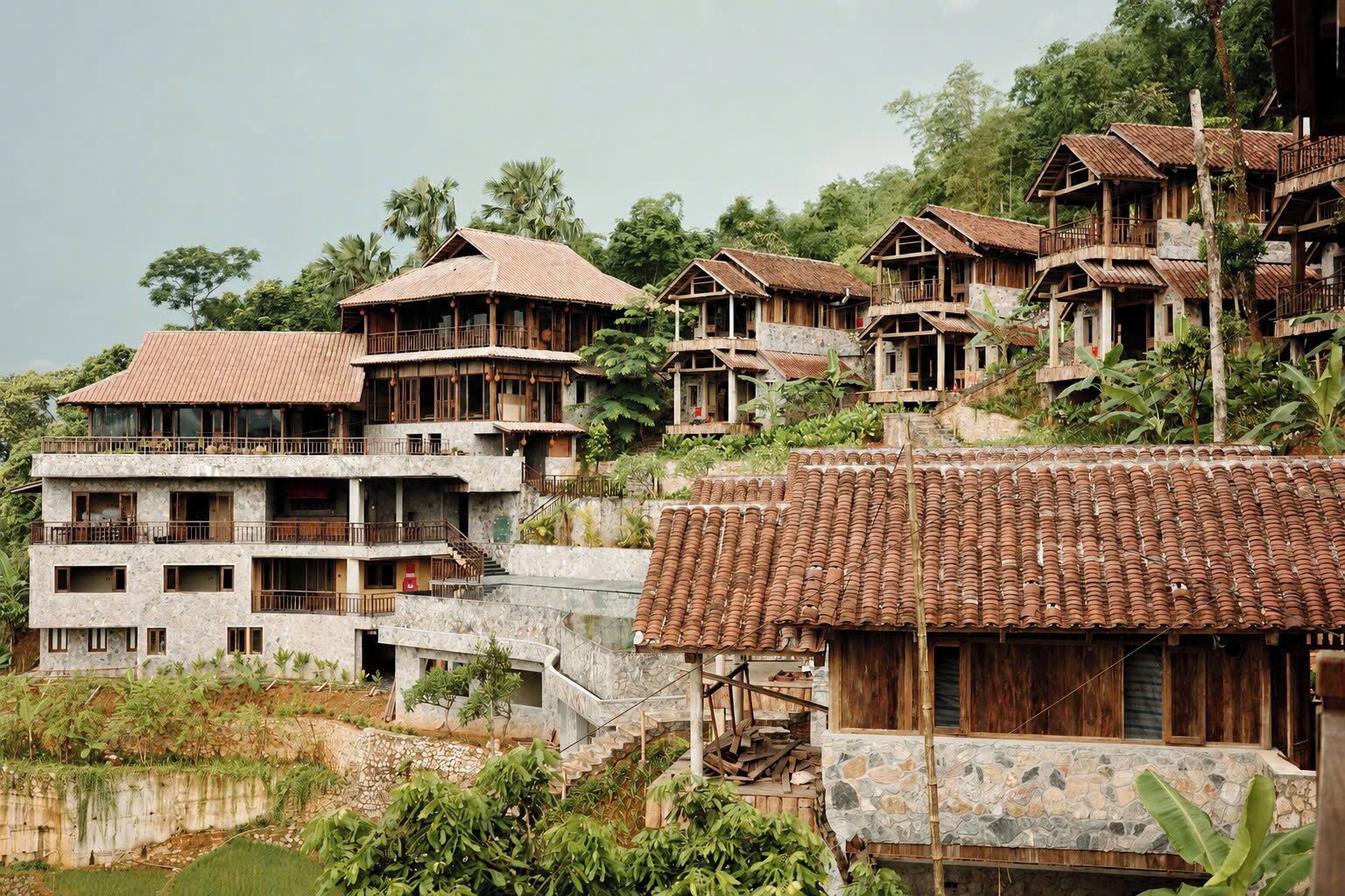 Ein an einem Hang gelegenes Dorf mit mehrstöckigen Holzhäusern, die Balkone aufweisen und eine Mischung aus Stein und Holz zeigen.