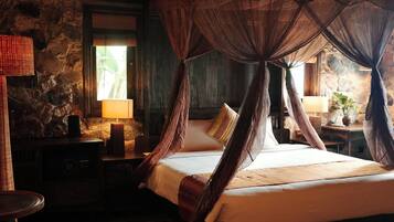 A bed with a canopy, a lamp, and a stone wall.