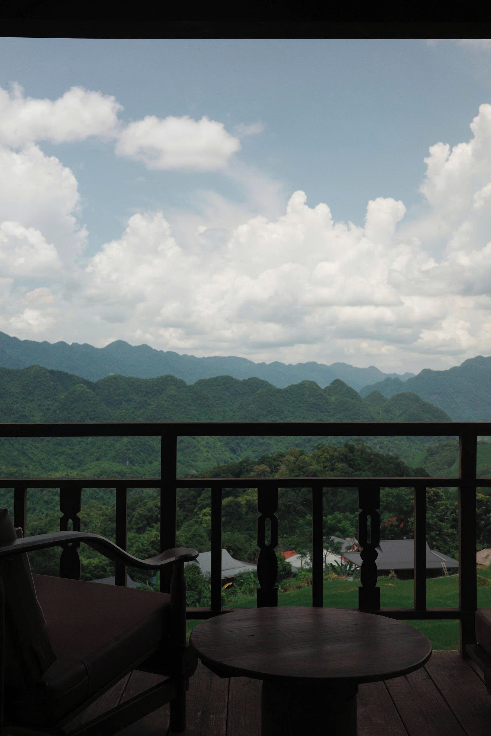 A wooden deck with a table and chairs, overlooking a mountainous landscape with a clear sky.