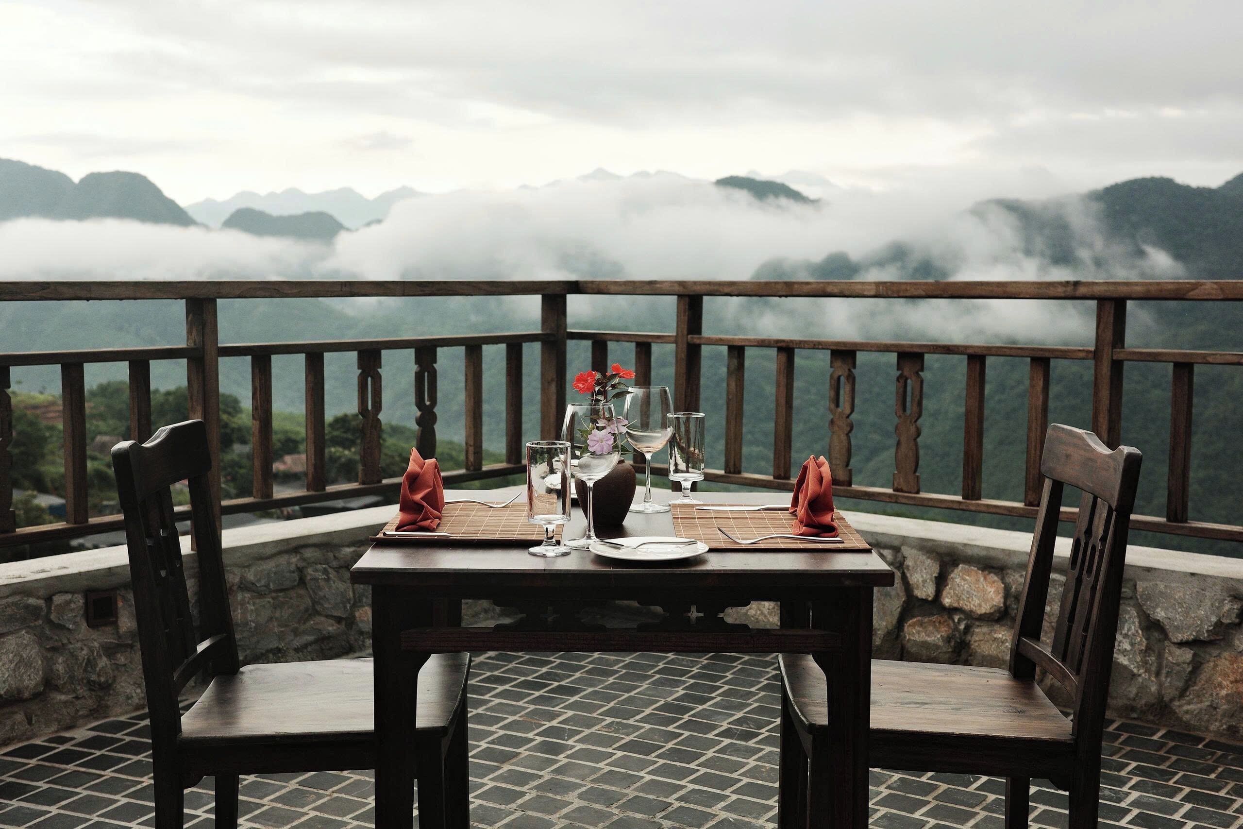A table set for two with a view of mountains and clouds.