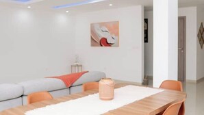 Uma sala de jantar moderna com uma mesa de madeira, cadeiras laranja, um tapete branco e um quadro na parede.