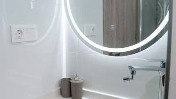 Un bany de disseny modern, amb un mirall rodó amb llum, un lavabo blanc i un panell de fusta al fons.