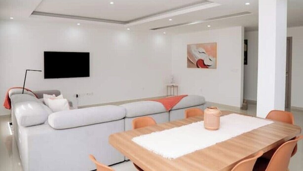 Uma sala de estar moderna com um sofá, uma mesa de jantar e uma TV de tela plana na parede.