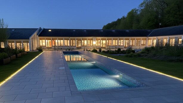 Ein modernes Haus mit Swimmingpool, gepflastertem Weg und gut beleuchteter Fassade.