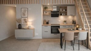 Eine moderne Küche mit einer Holztreppe, weißen Schränken und einem Essbereich mit zwei Stühlen.
