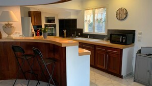 Une cuisine moderne avec un îlot central aux lignes courbes, des armoires en bois, un four à micro-ondes et une horloge murale.