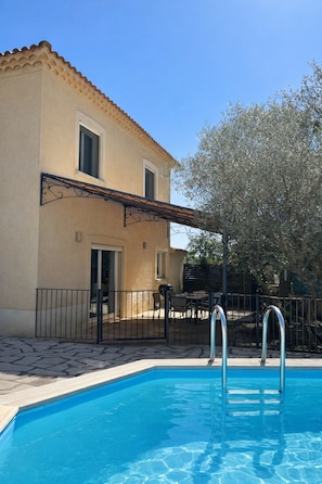 Ein Pool mit zwei Leitern, ein Gebäude mit einem Ziegeldach und ein Baum.