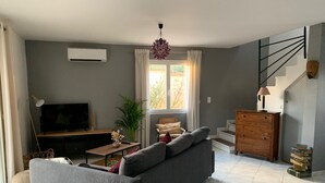Un salon avec un canapé gris, un téléviseur, une plante et un escalier.
